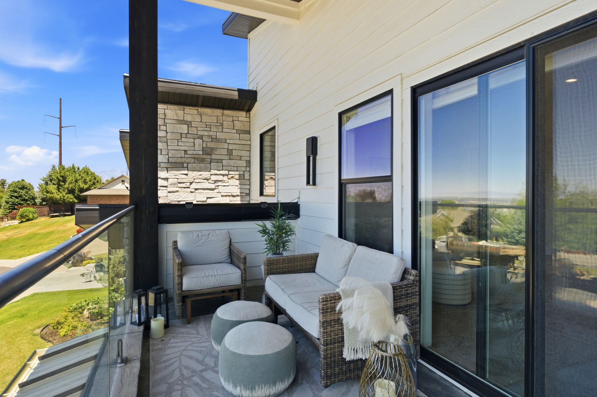 Private outdoor balcony featuring a glass railing, white horizontal siding, stone accent wall, and a large sliding glass door