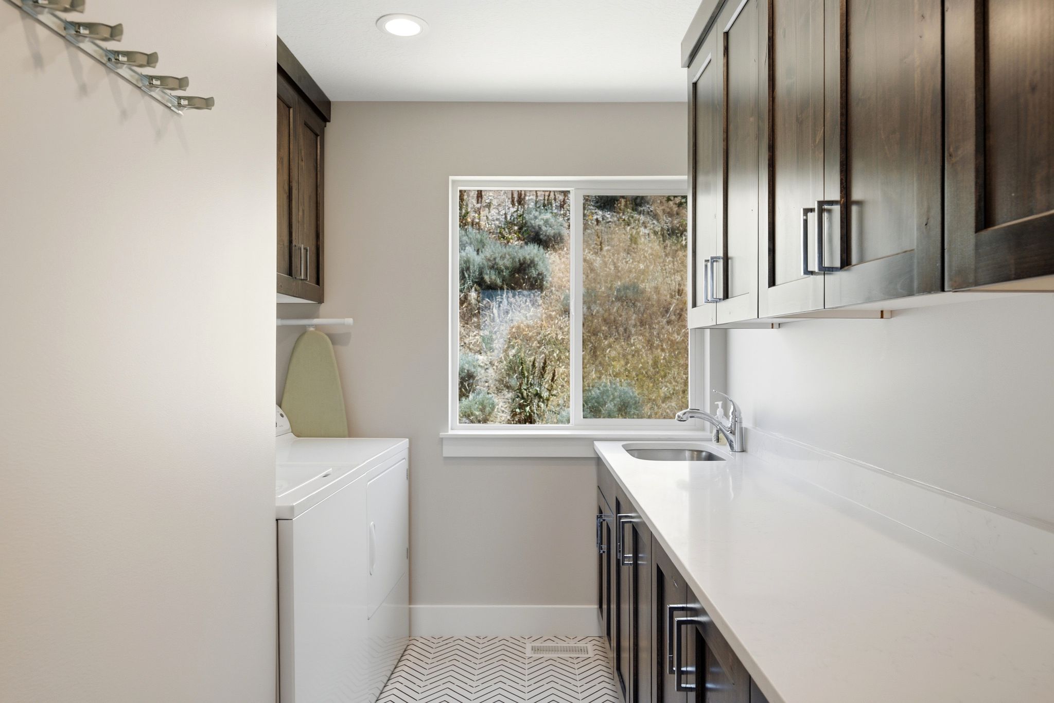 Laundry room with a window, white countertops, built-in sink, dark wood-finish cabinetry, and chevron patterned flooring