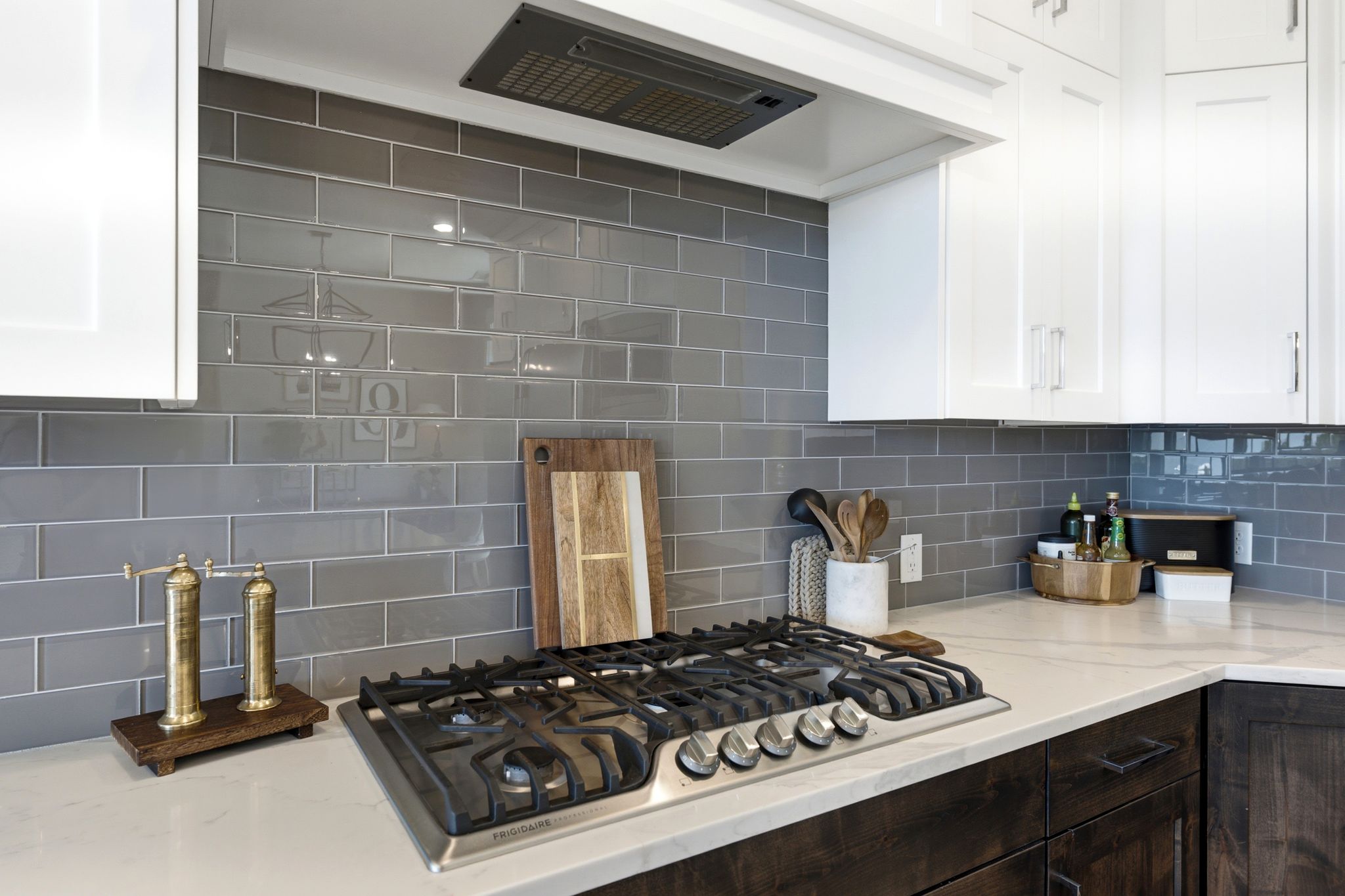 Modern kitchen featuring a built-in gas range, white upper cabinetry, dark wood-finish lower cabinetry, and a grey subway tile backsplash
