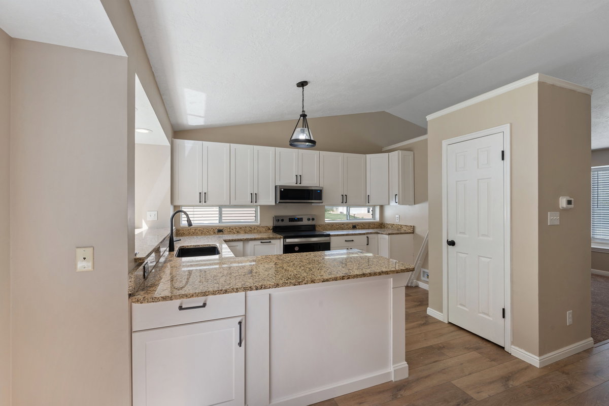 Modern kitchen featuring white cabinetry, granite countertops, wood-finish flooring, a black sink with a gooseneck faucet, and stainless steel appliances including a built-in microwave