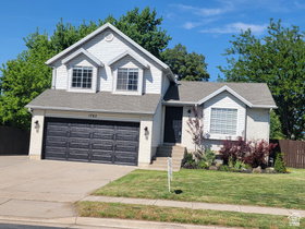 Two-story residential structure featuring a two-car garage with paneling, a front-facing dormer with two windows, and established landscaping
