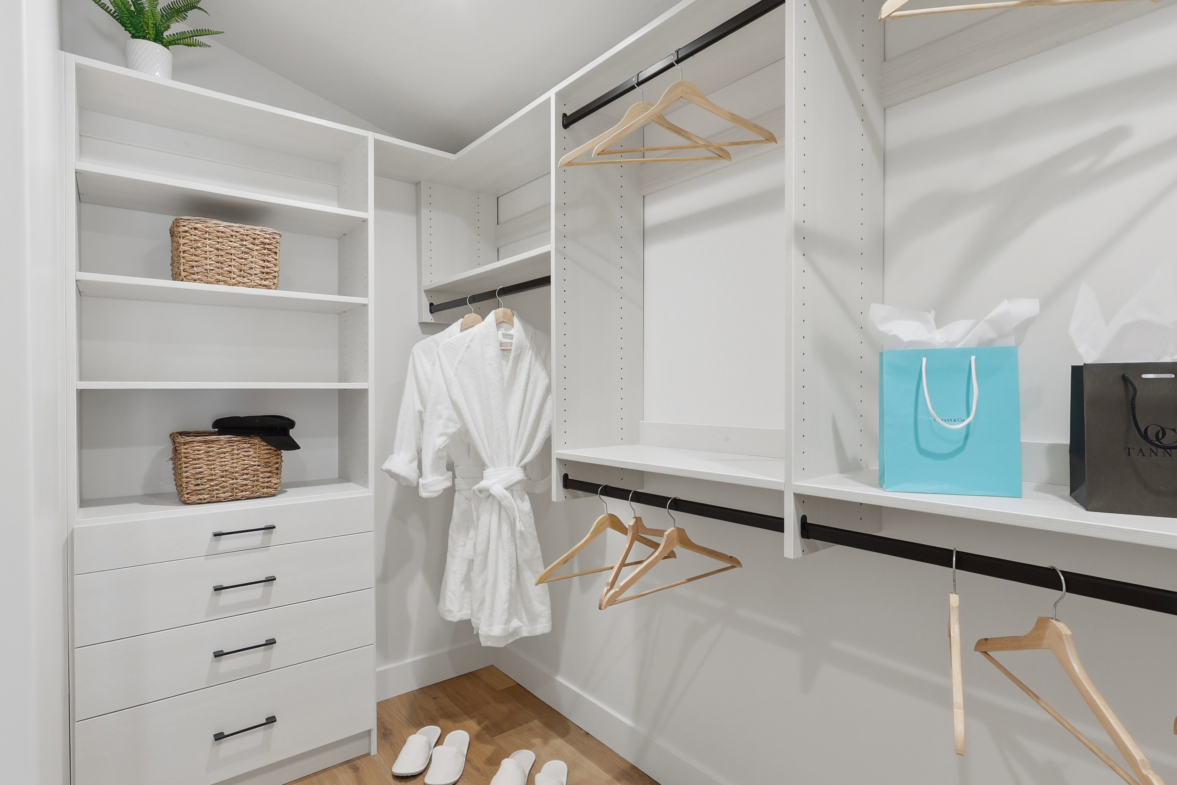 Custom-designed closet system featuring white shelving, multiple hanging rods, and integrated drawer storage with matte black hardware