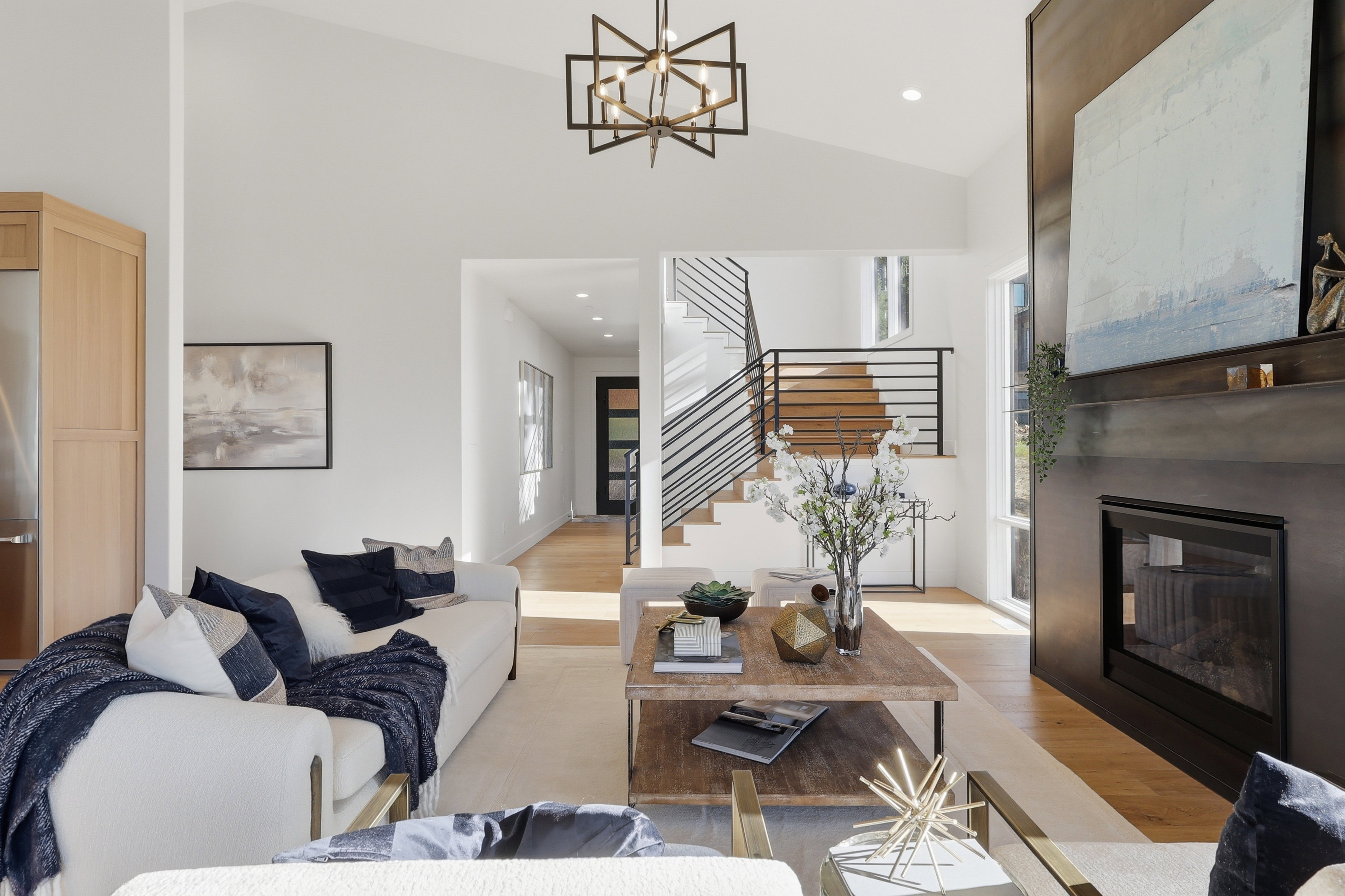 Vaulted ceiling living area featuring a modern fireplace, wood-finish flooring, a contemporary chandelier, and a staircase with open risers and horizontal metal railings