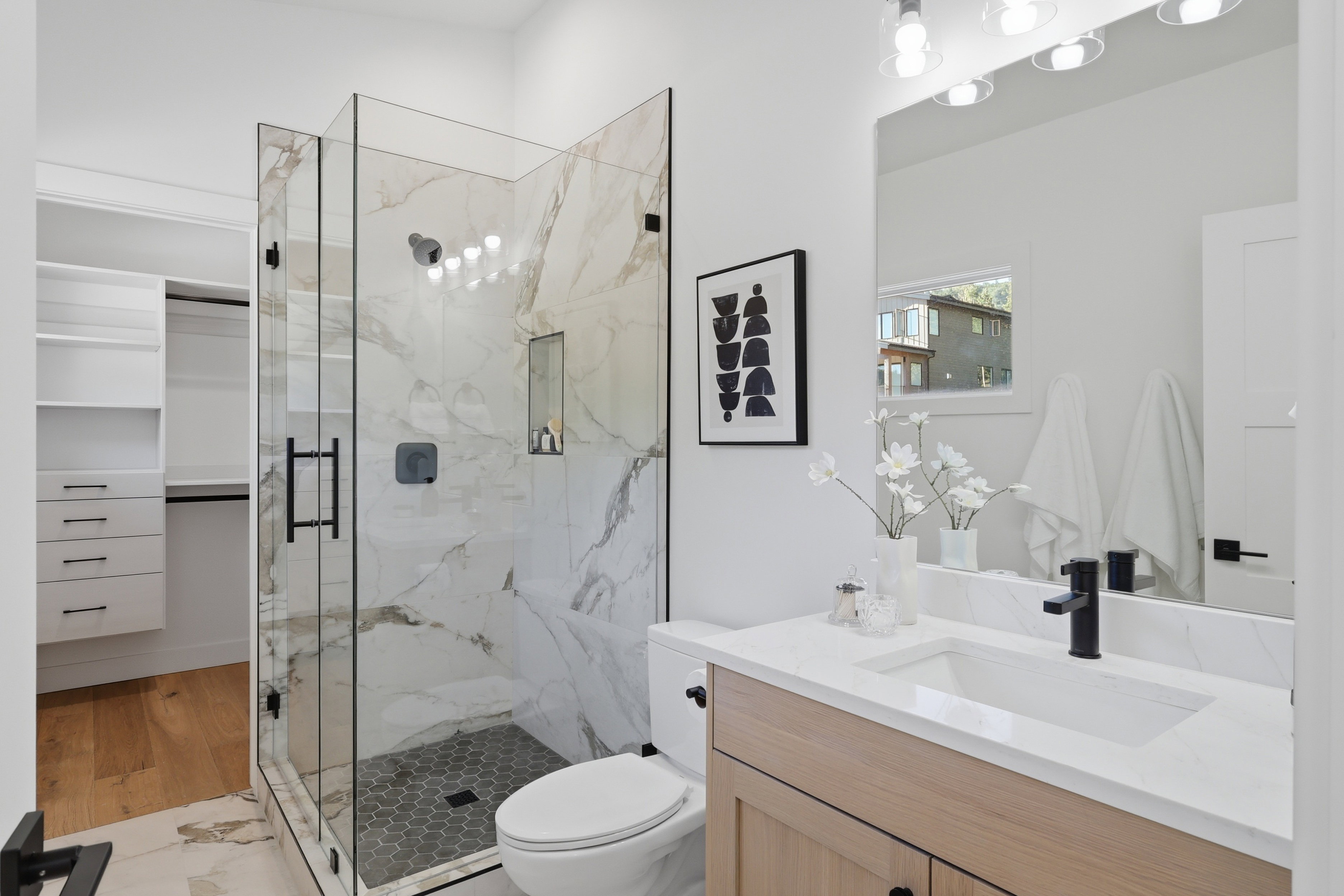 Modern bathroom featuring a glass-enclosed shower with marble-look tile, a built-in shower niche, and a hexagonal tile floor