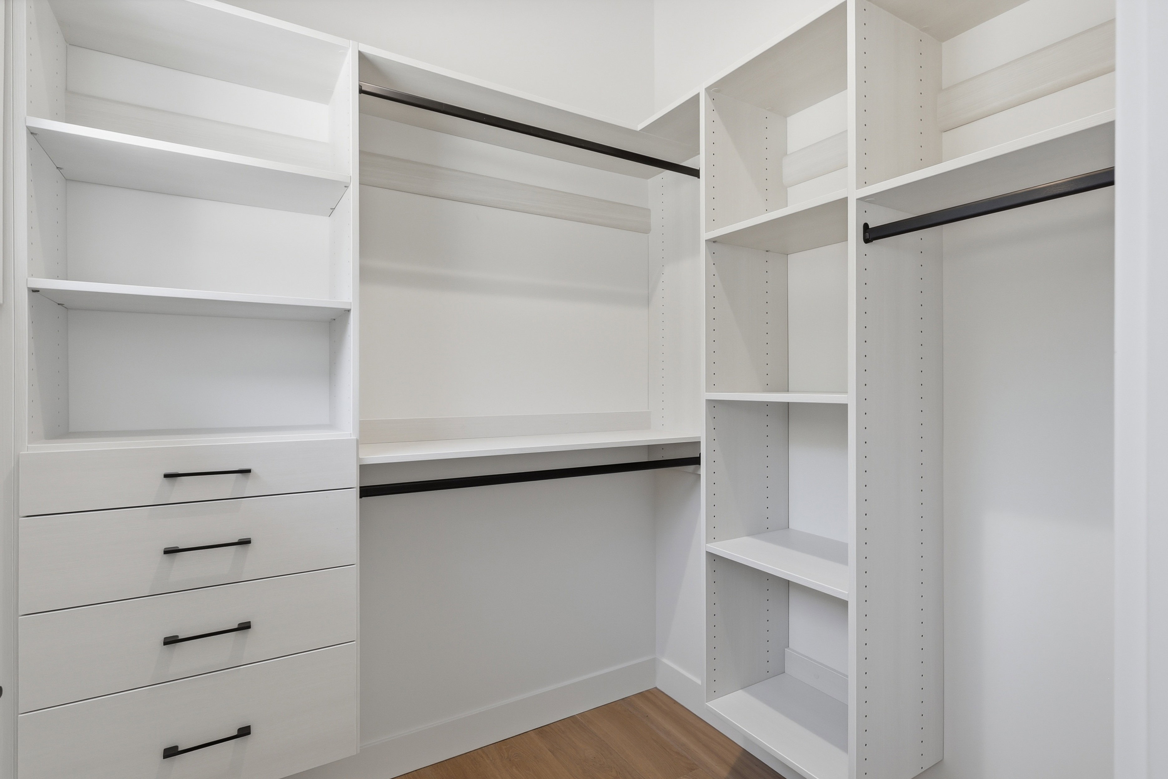 Custom closet system featuring multiple hanging rods, adjustable shelving, and integrated drawers with contemporary black hardware