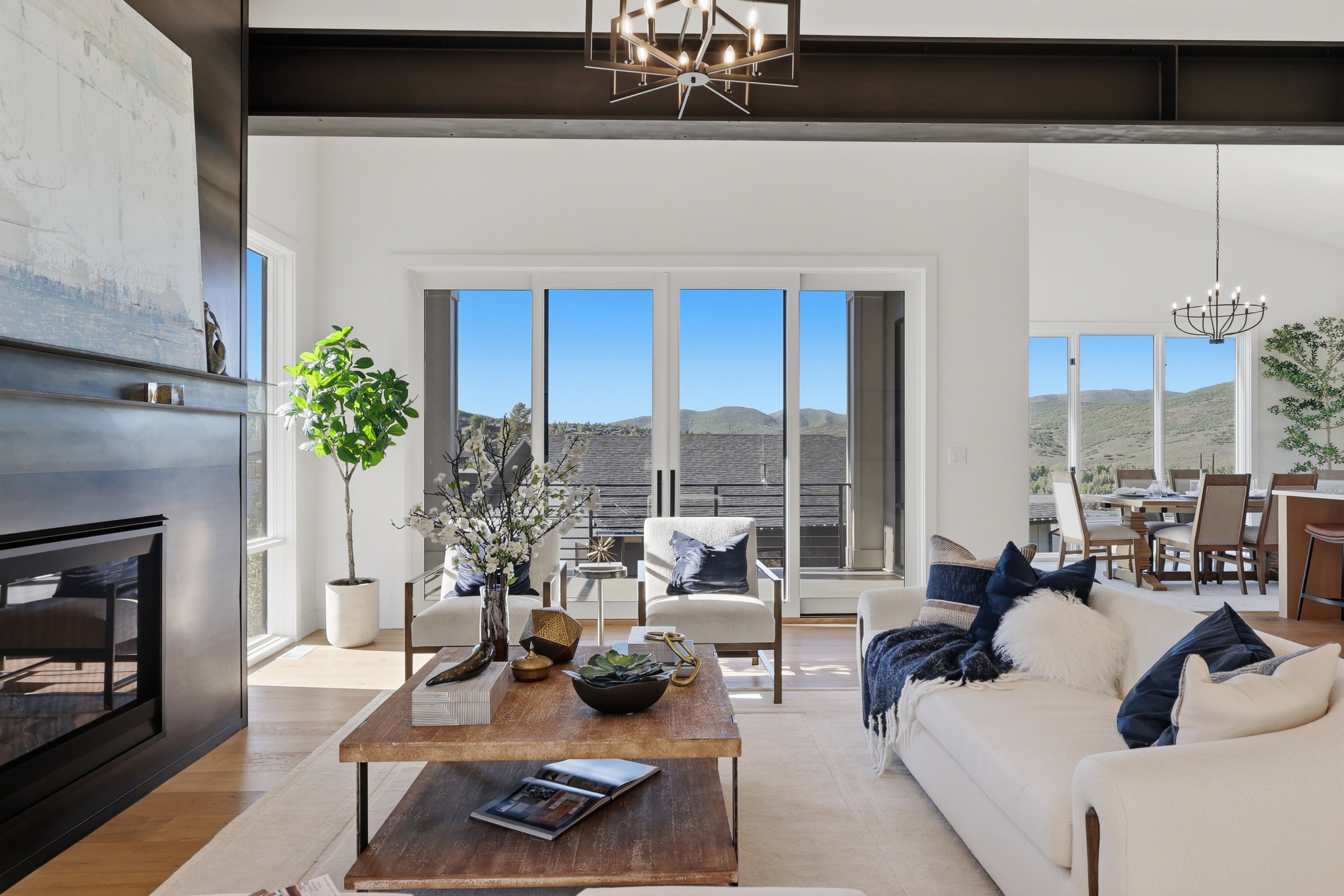 Spacious living area featuring a modern fireplace, exposed structural beams, light wood-finish flooring, and multiple glass sliding doors