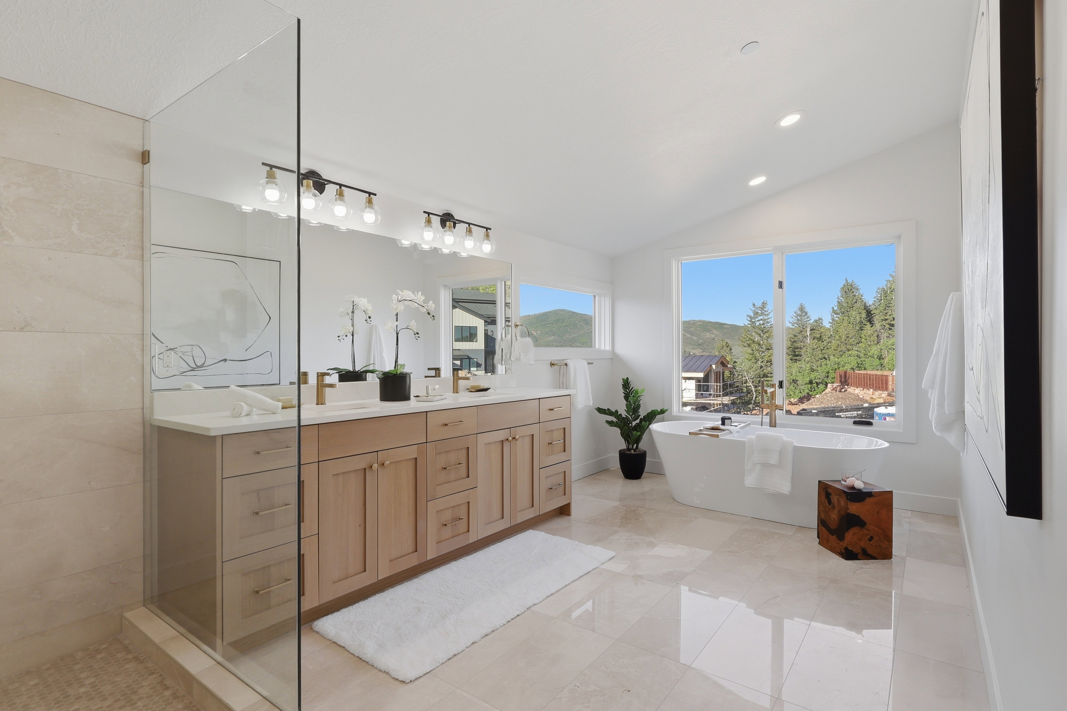 Spacious bathroom featuring a freestanding soaking tub, dual sink vanity with light wood cabinetry, and a walk-in glass-enclosed shower