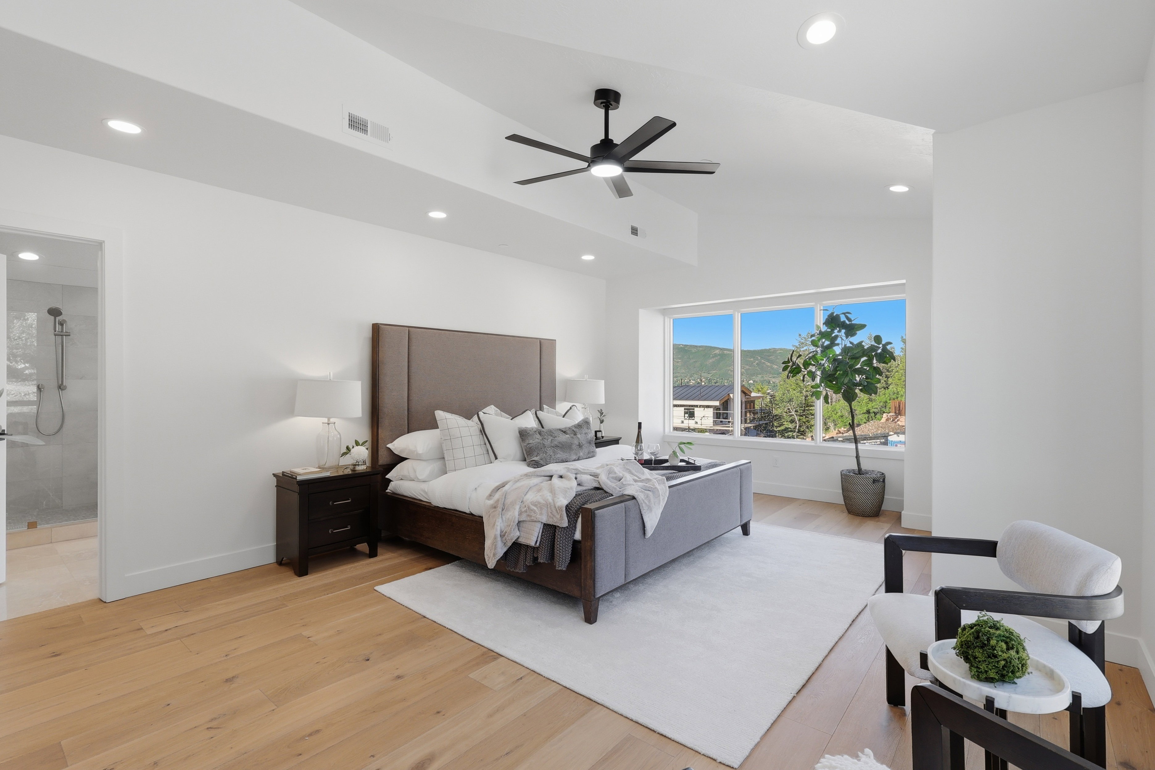 Spacious bedroom featuring light wood-finish flooring, a large window, recessed lighting, a ceiling fan, and an en-suite bathroom with a glass-enclosed shower