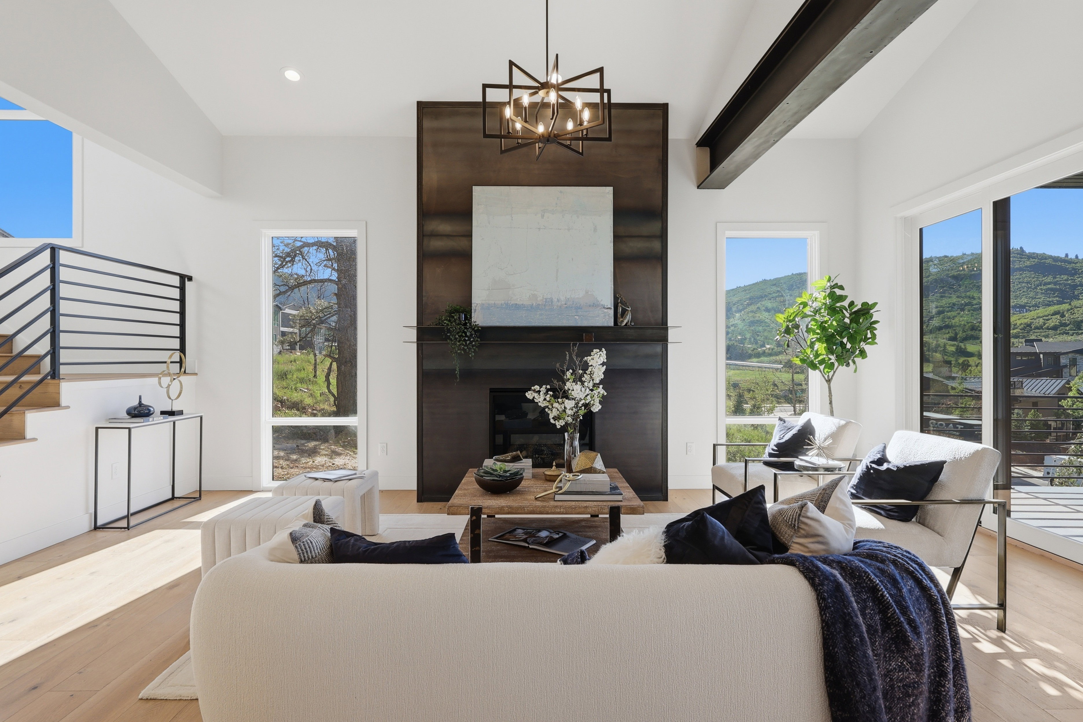 Vaulted ceiling living space featuring a floor-to-ceiling fireplace with a dark finish, large windows, wood-finish flooring, and a modern chandelier