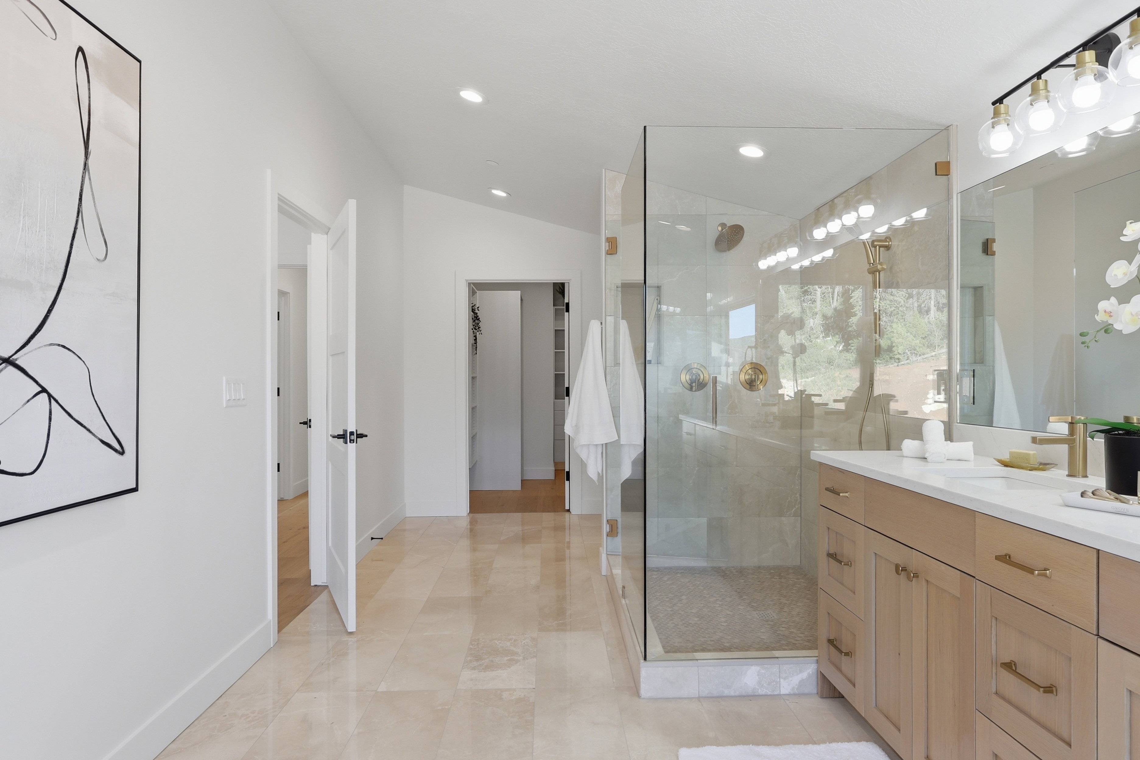 Spacious bathroom featuring a frameless glass shower enclosure, dual vanity with light wood cabinetry, recessed lighting, and large format tile flooring