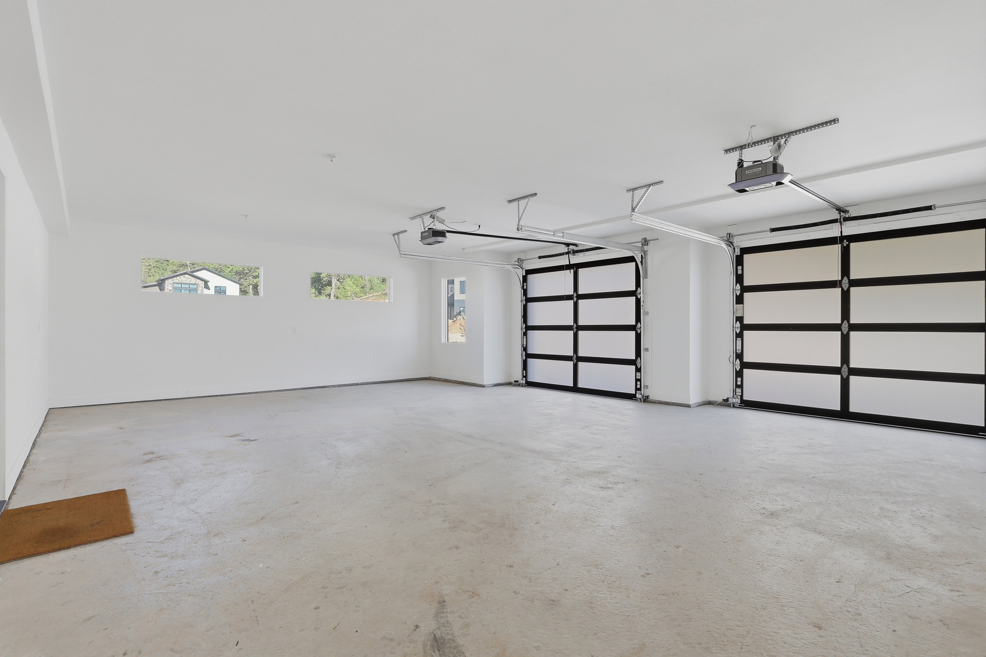 Spacious garage featuring two modern glass-paneled garage doors, a concrete floor, and multiple windows providing natural light