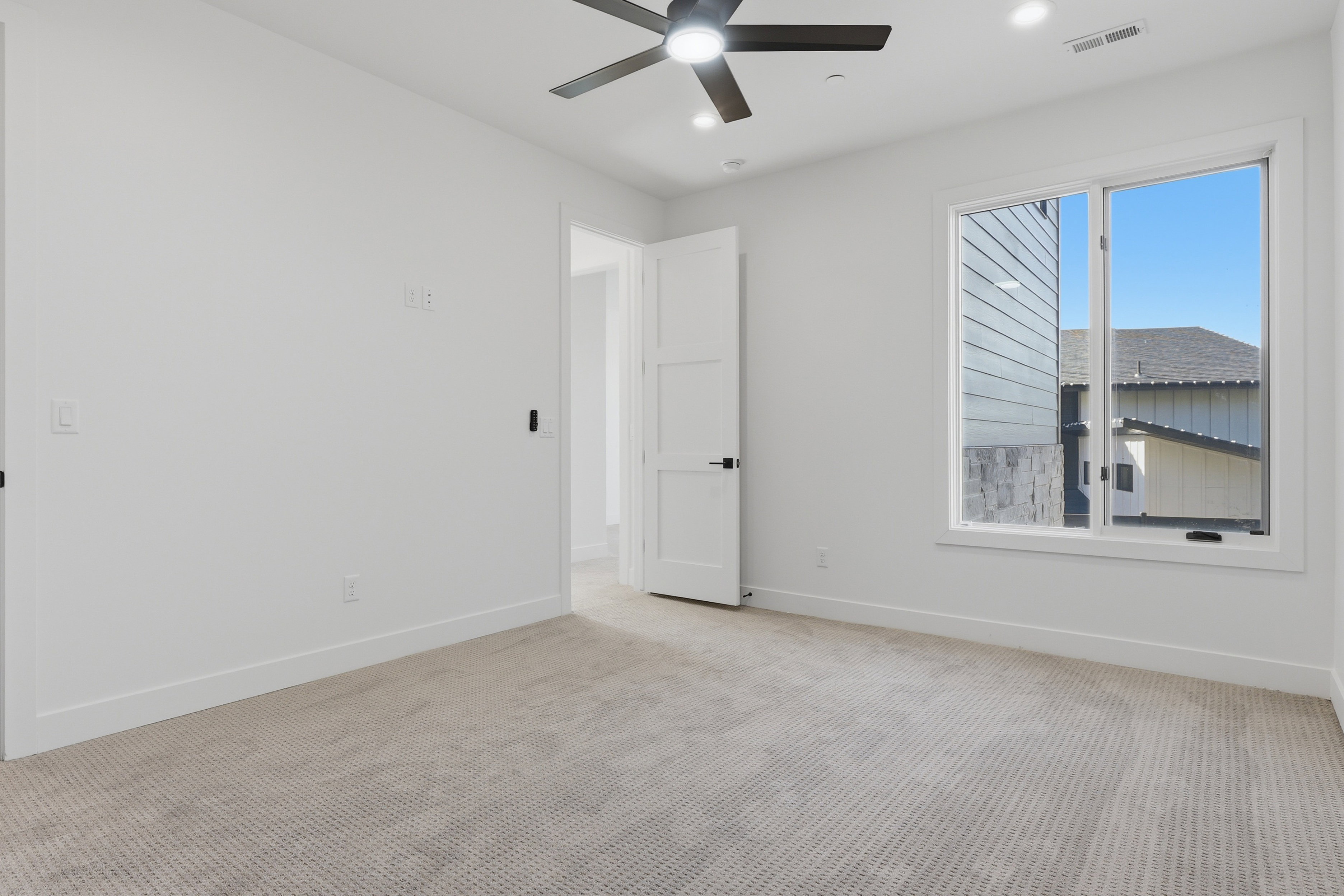 Spacious room featuring neutral carpeting, white walls, a large window, a modern ceiling fan with integrated lighting, and recessed ceiling lights