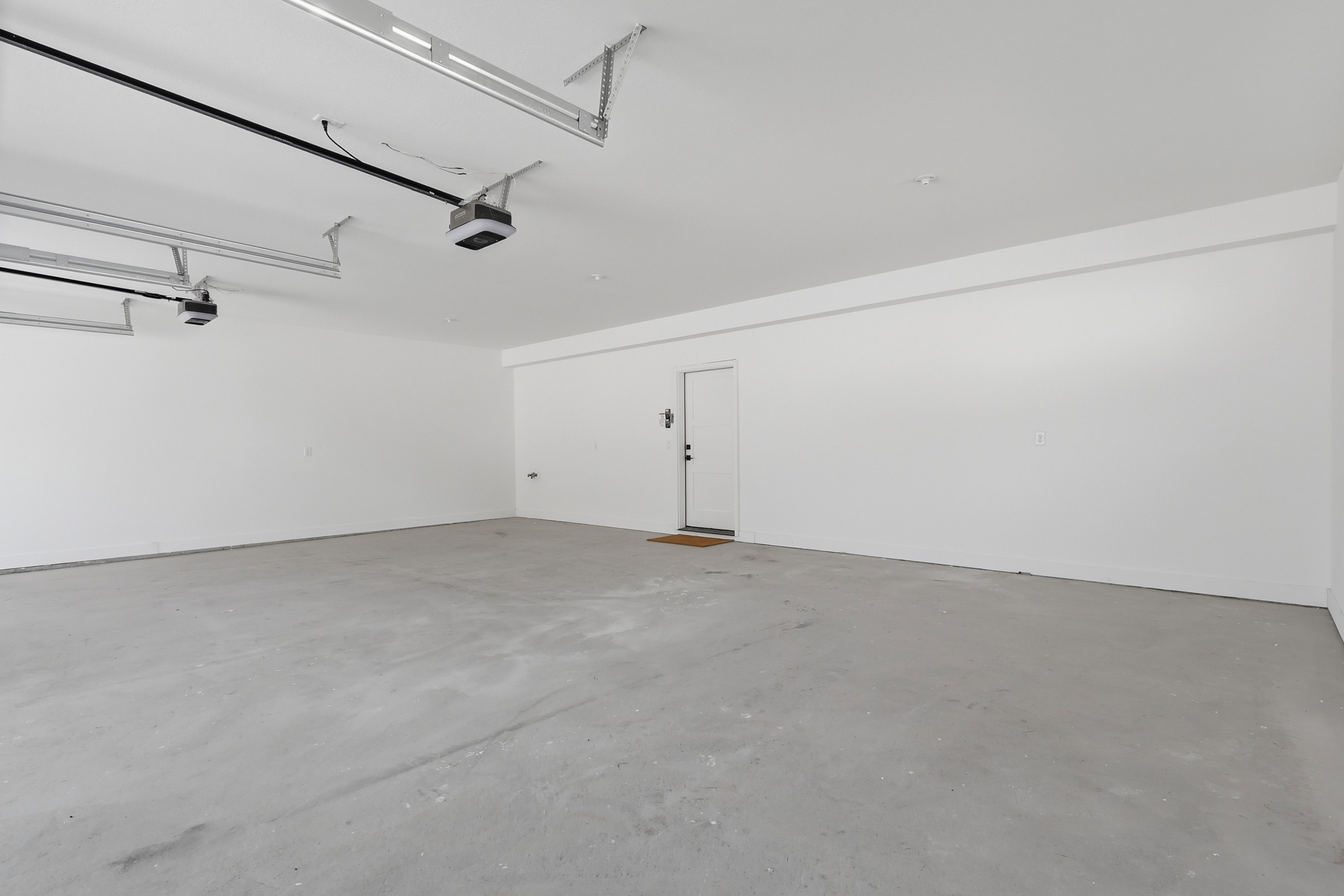 Spacious garage featuring a concrete floor, bright white walls, and two overhead garage door openers
