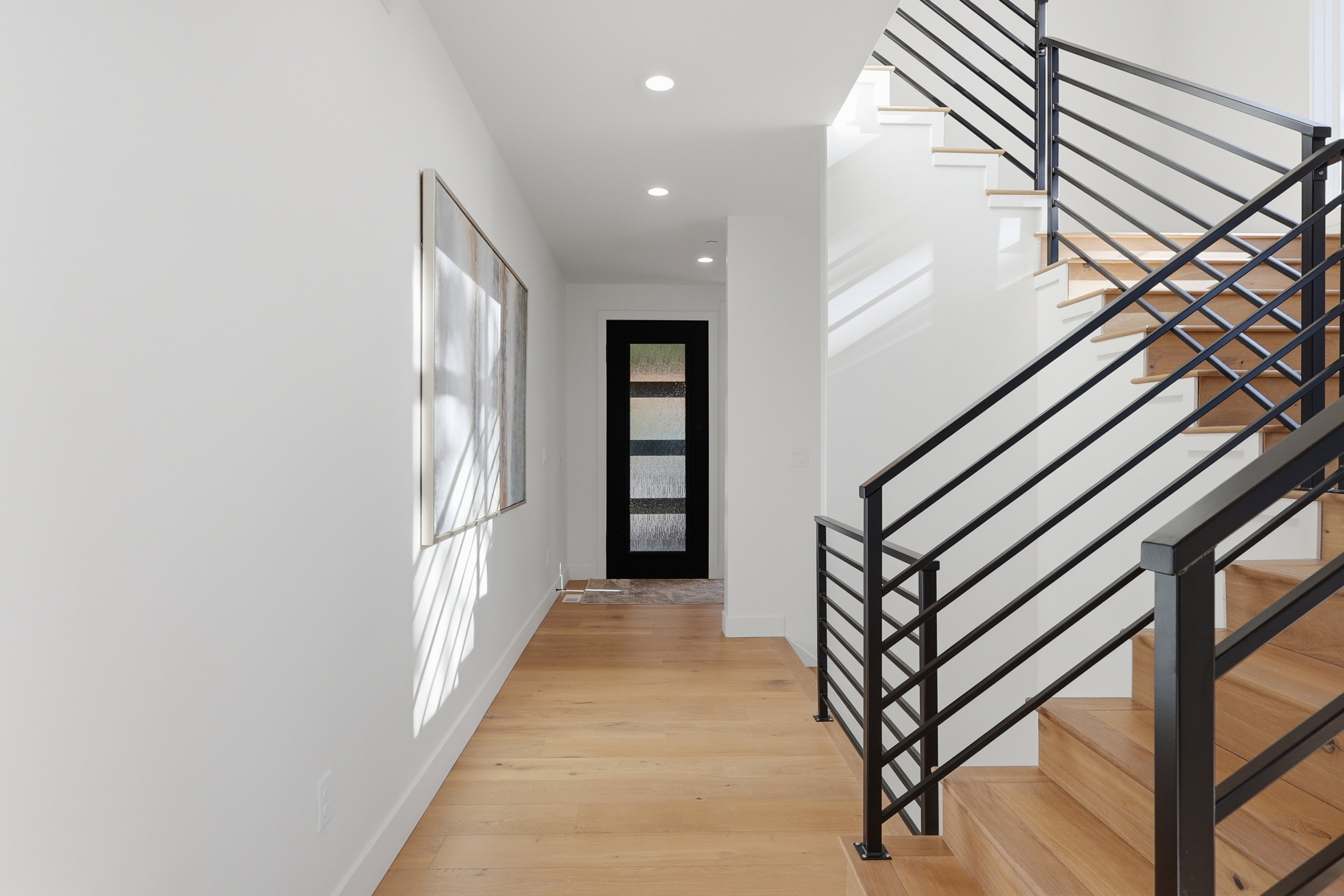 Entryway featuring a modern staircase with black metal railings, recessed lighting, wood-finish flooring, and a contemporary glass-paneled door