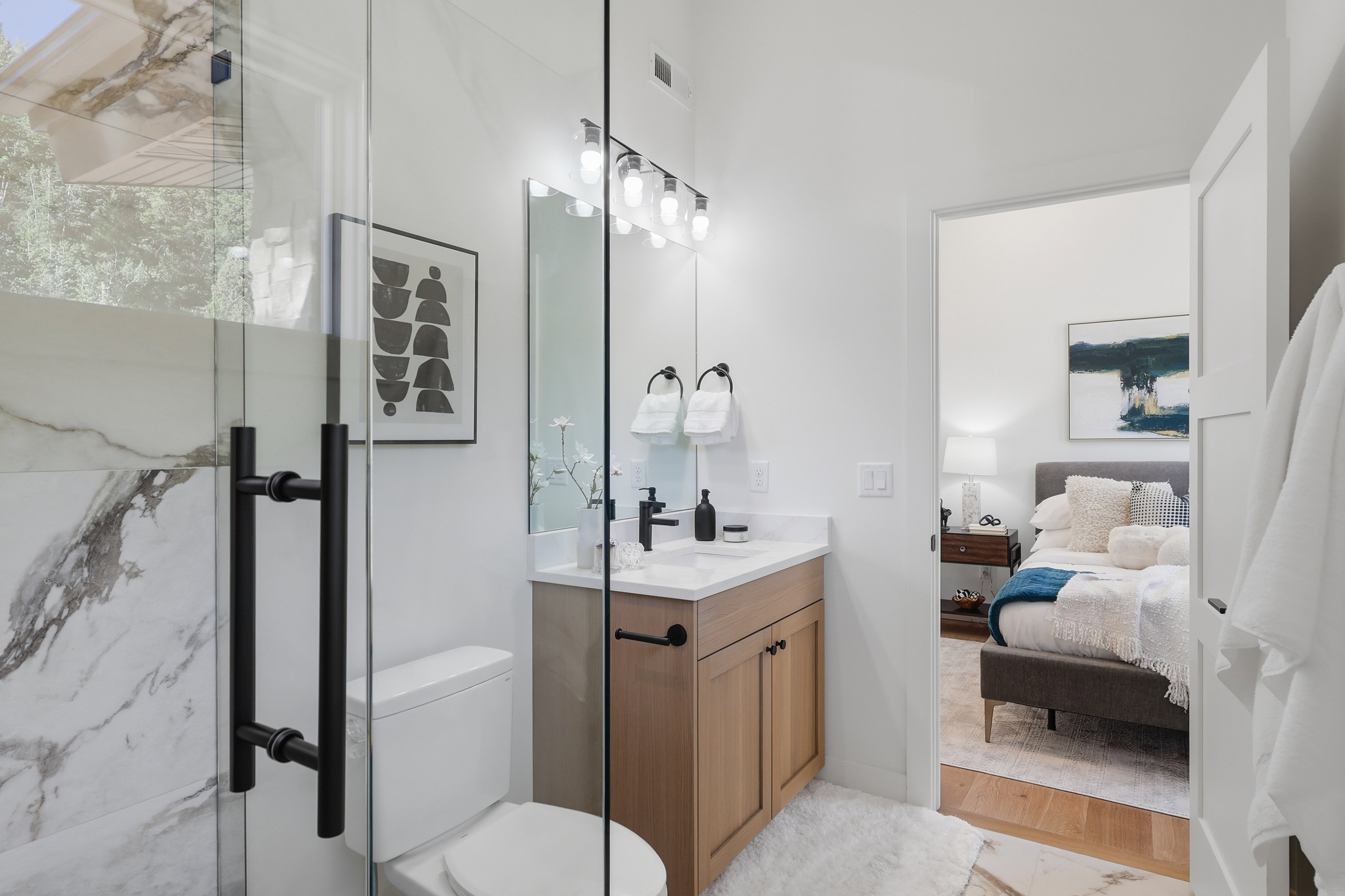 Modern bathroom featuring a glass-enclosed shower with matte black hardware, a wood-finish vanity with a white countertop, and a contemporary light fixture above the mirror