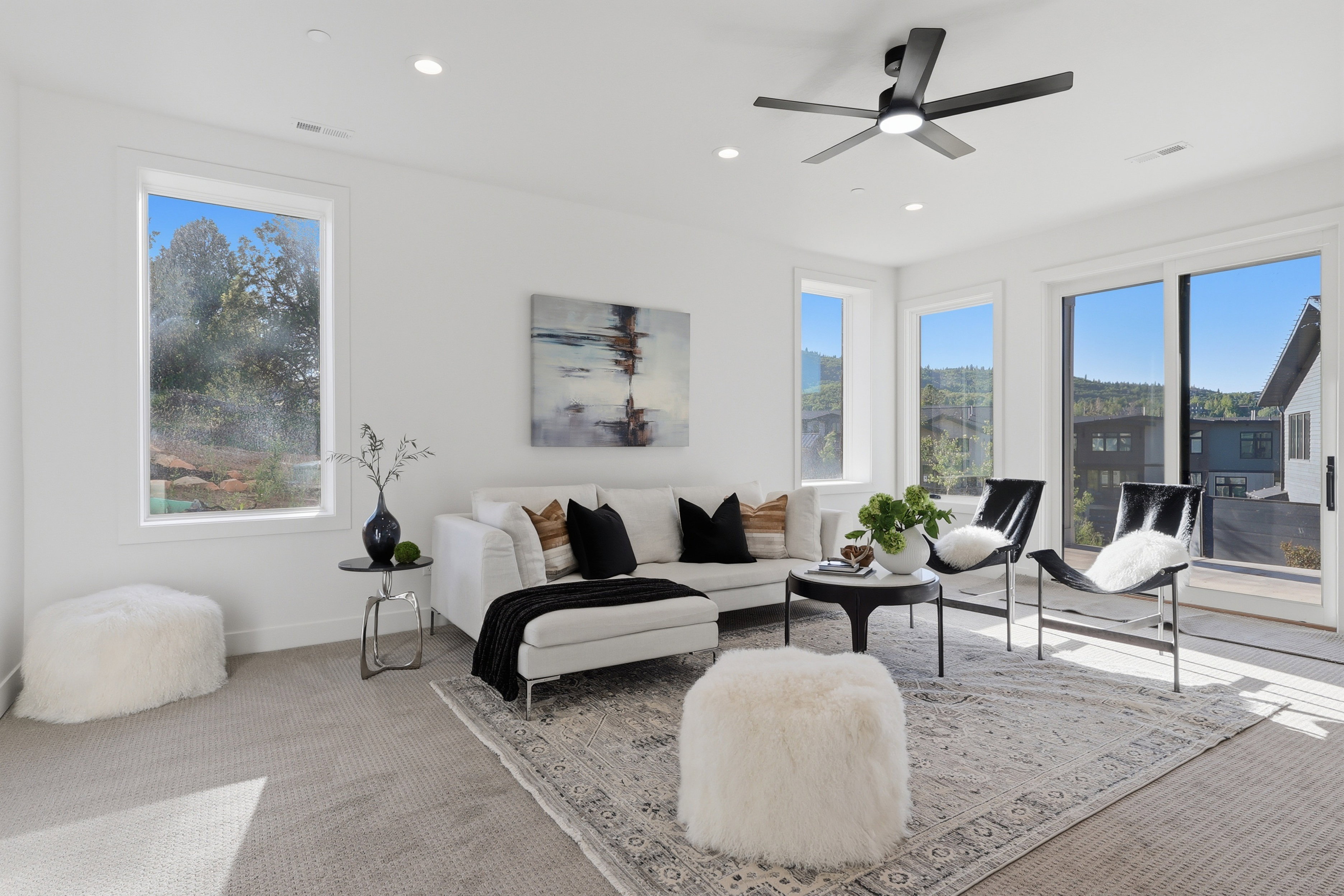 Spacious living area featuring light-toned carpeting, white walls, multiple windows, and a sliding glass door