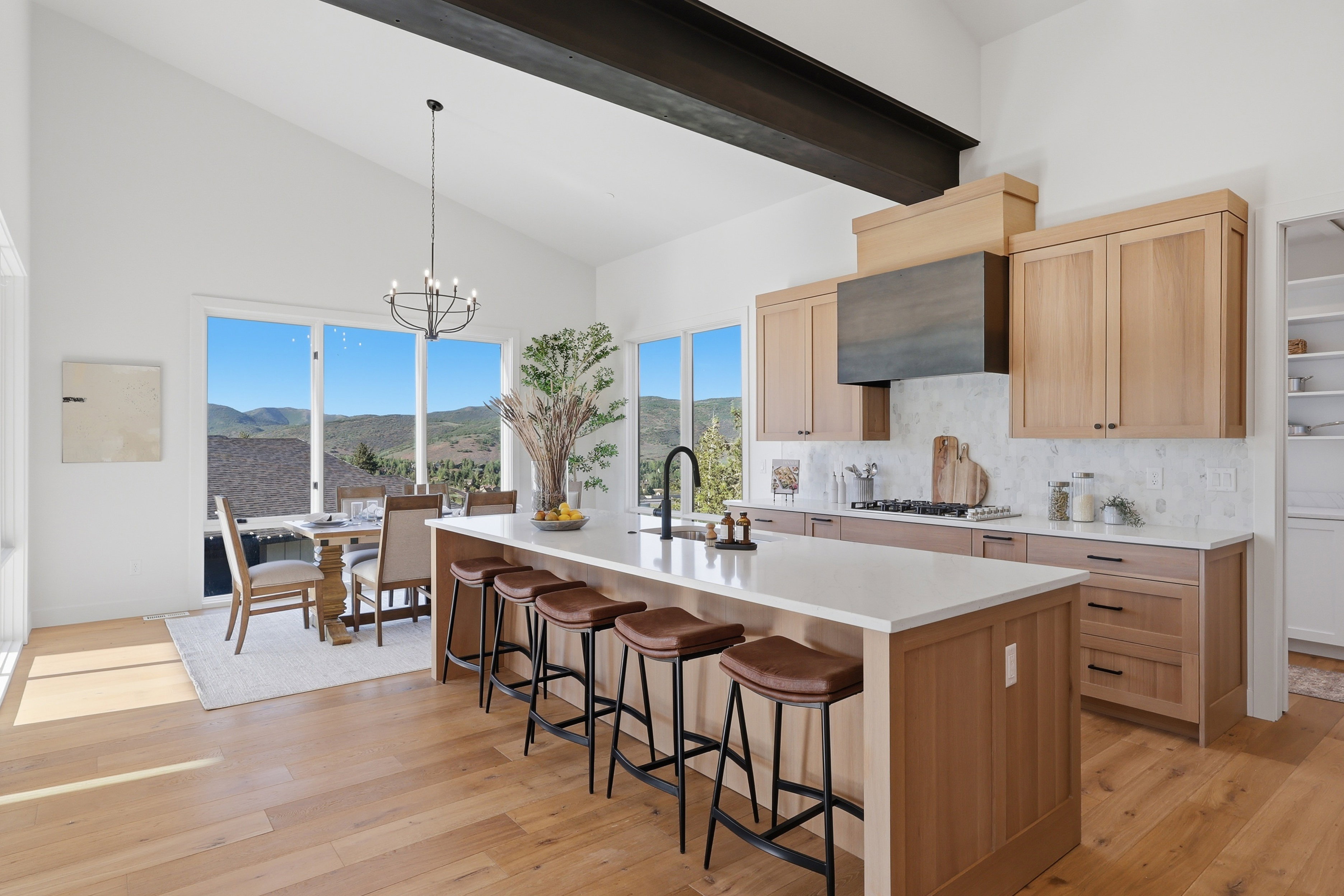 Open-concept kitchen and dining area featuring vaulted ceilings with an exposed beam, light wood-finish flooring, and large windows