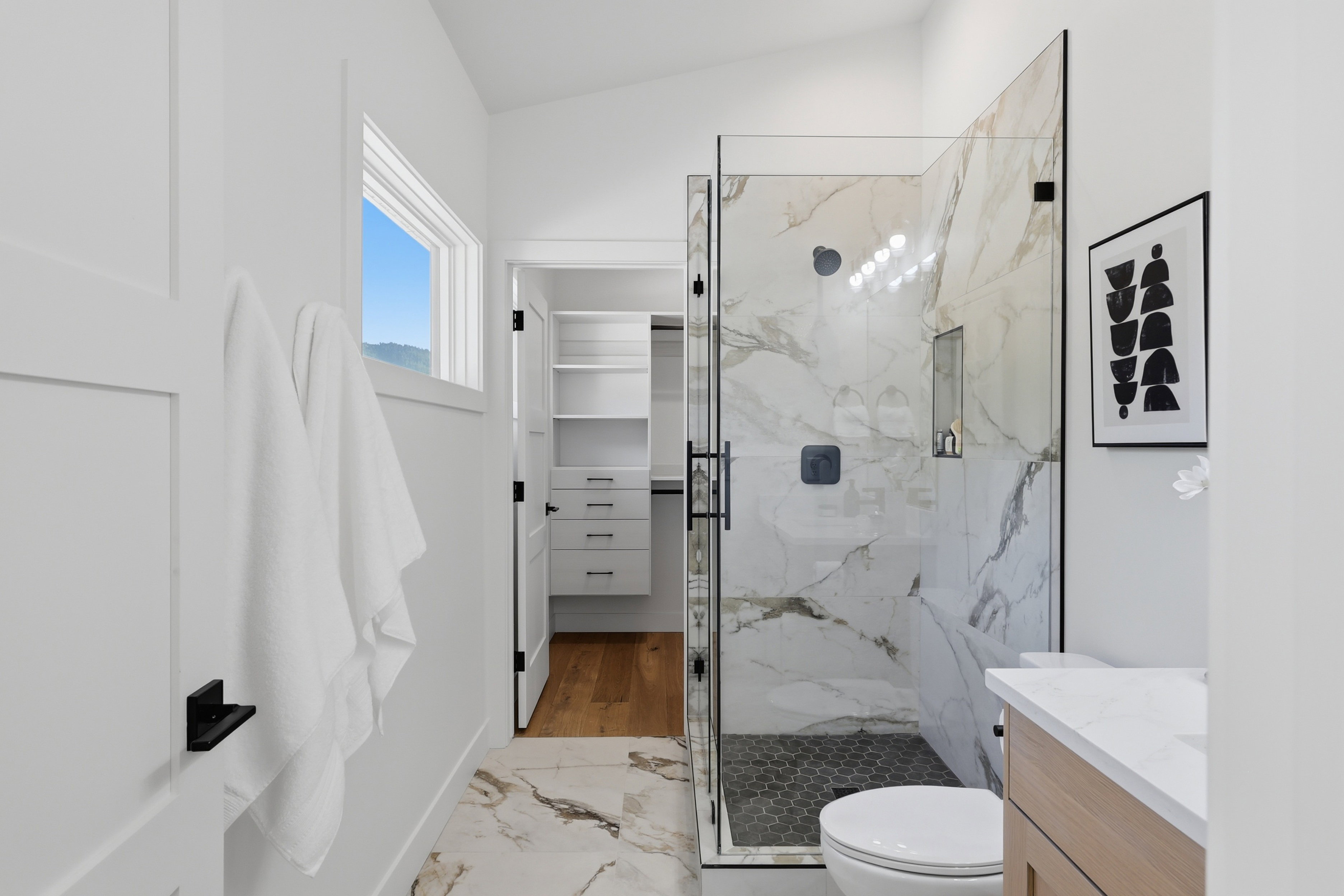 Glass-enclosed shower with a marble-effect tile surround and a hexagonal dark-tiled floor