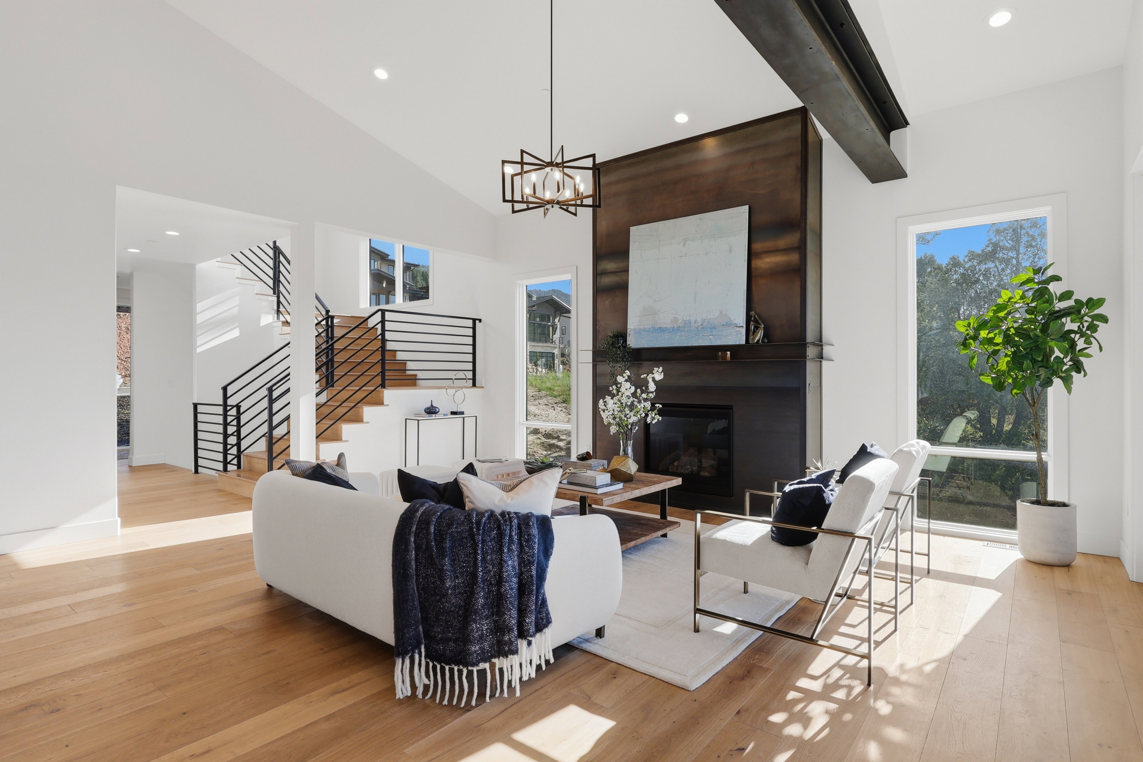 Vaulted living space featuring wood-finish flooring, a contemporary chandelier, and a fireplace with a dark metal surround