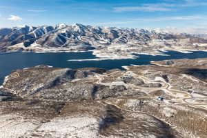 Expansive mountain landscape featuring a large lake, snow-dusted terrain, and winding roads