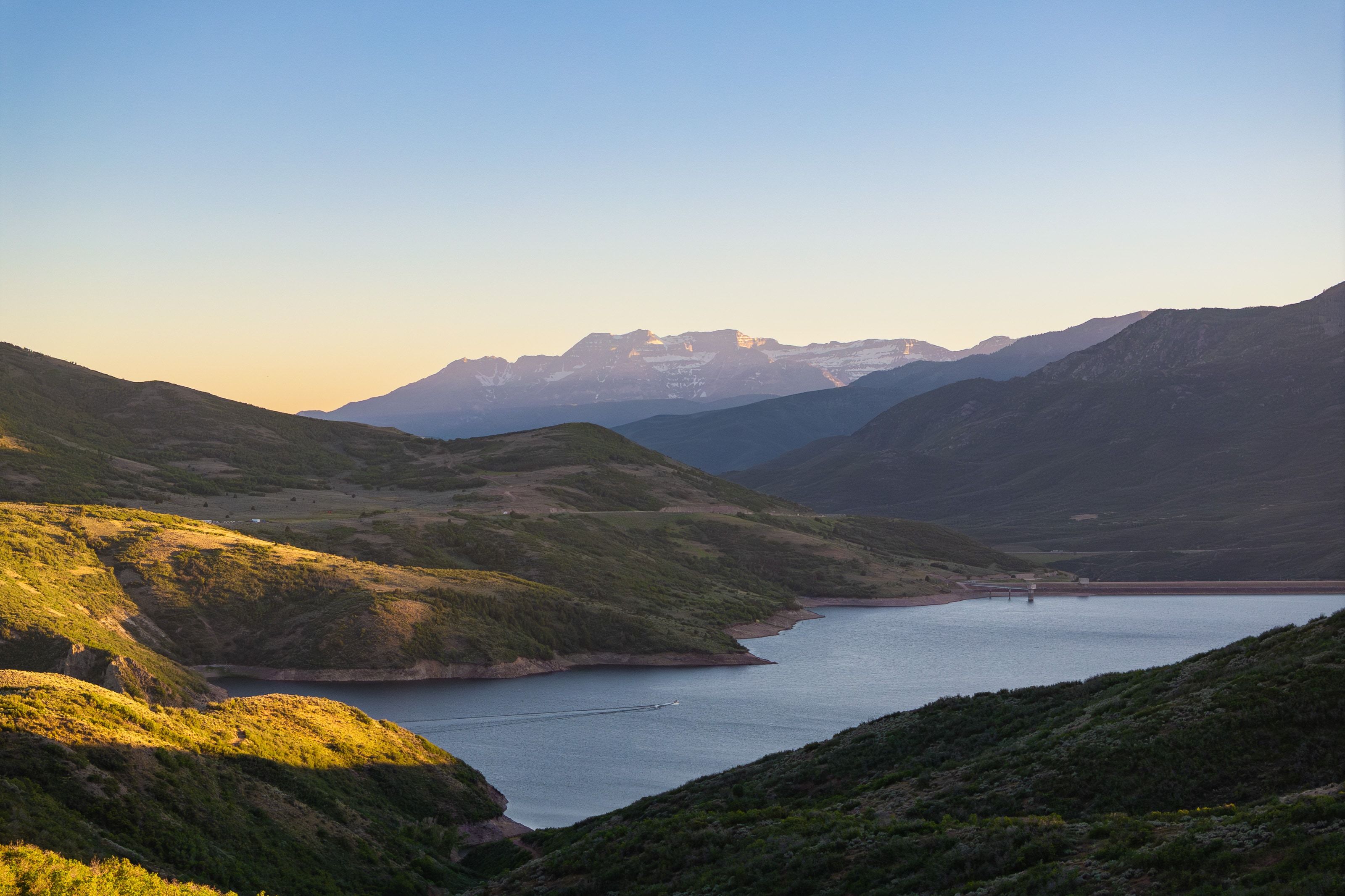 Expansive mountain landscape featuring a large body of water, rolling hillsides, and distant peaks