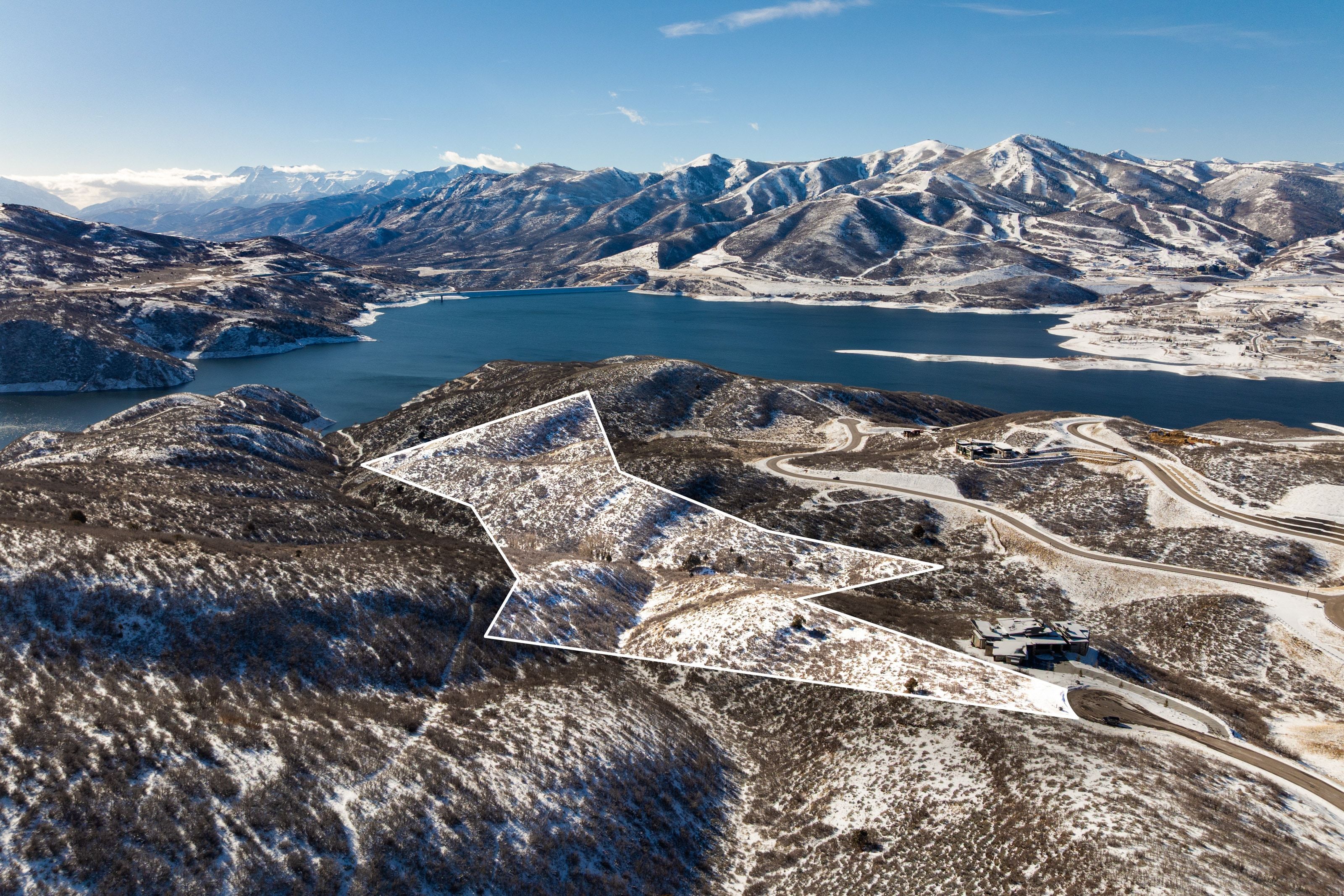 Expansive land parcel outlined against a backdrop of snow-dusted mountains and a substantial body of water