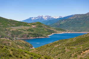 Expansive lake and mountain landscape featuring a deep blue lake, lush green hillsides, and snow-capped peaks in the distance