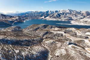 Expansive mountain landscape featuring a large body of water, snow-dusted terrain, and winding roads