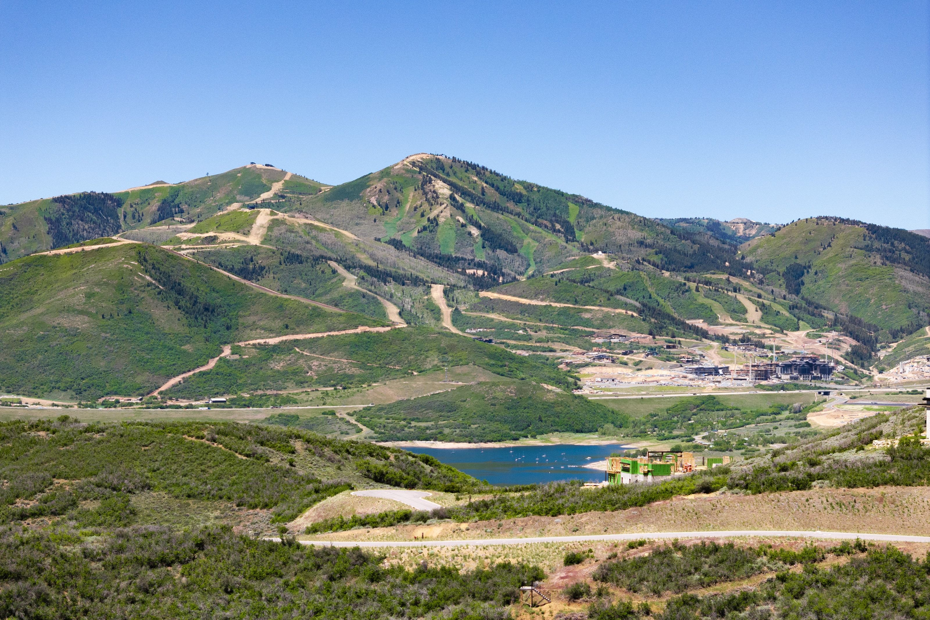 Expansive mountainous terrain featuring ski runs, verdant hillsides, and a prominent lake