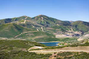 Expansive mountainous terrain featuring ski runs, verdant hillsides, and a prominent lake
