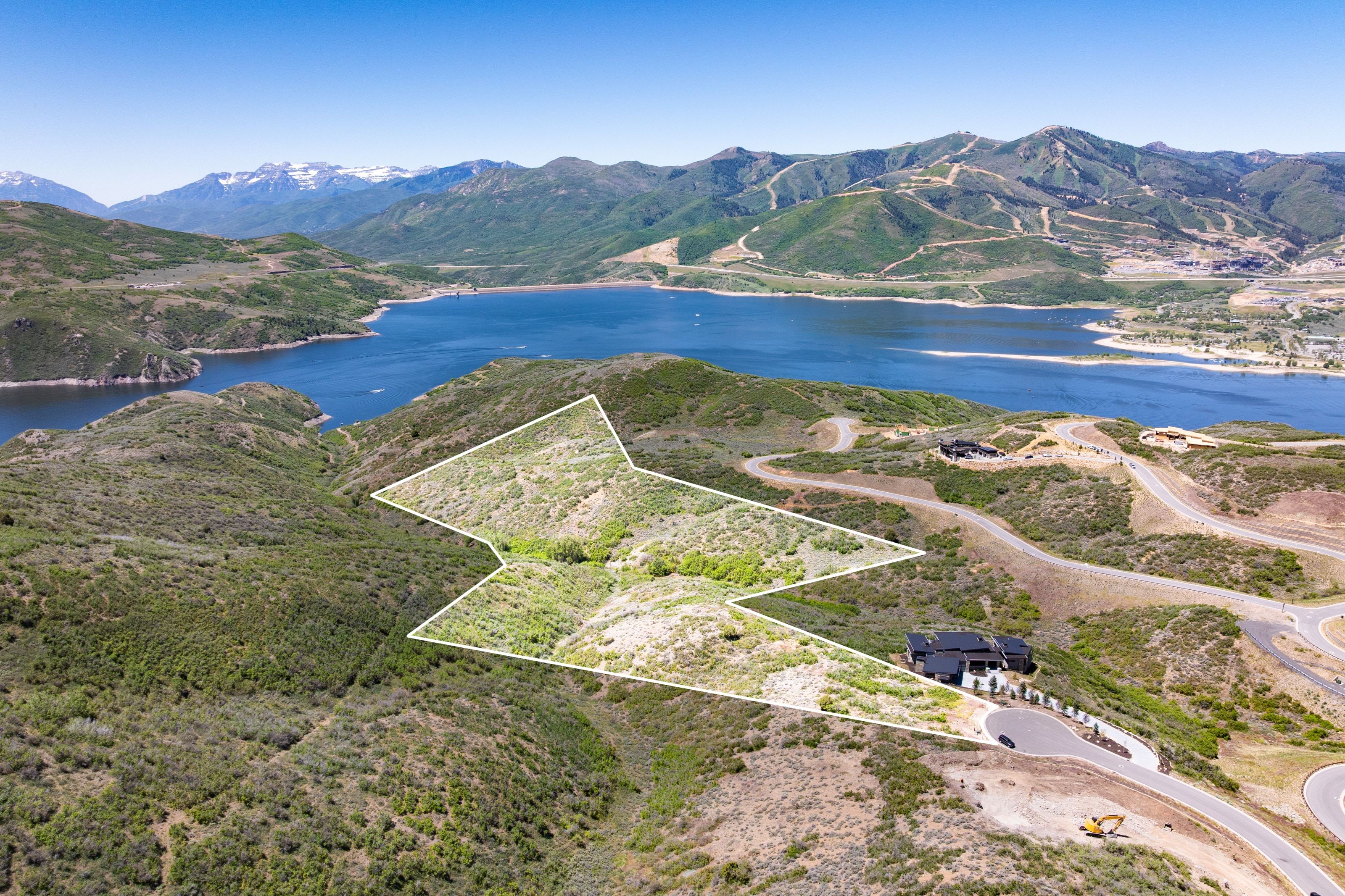 Expansive hillside lot featuring natural vegetation, a distinct lot boundary, a paved road, and mountain scenery