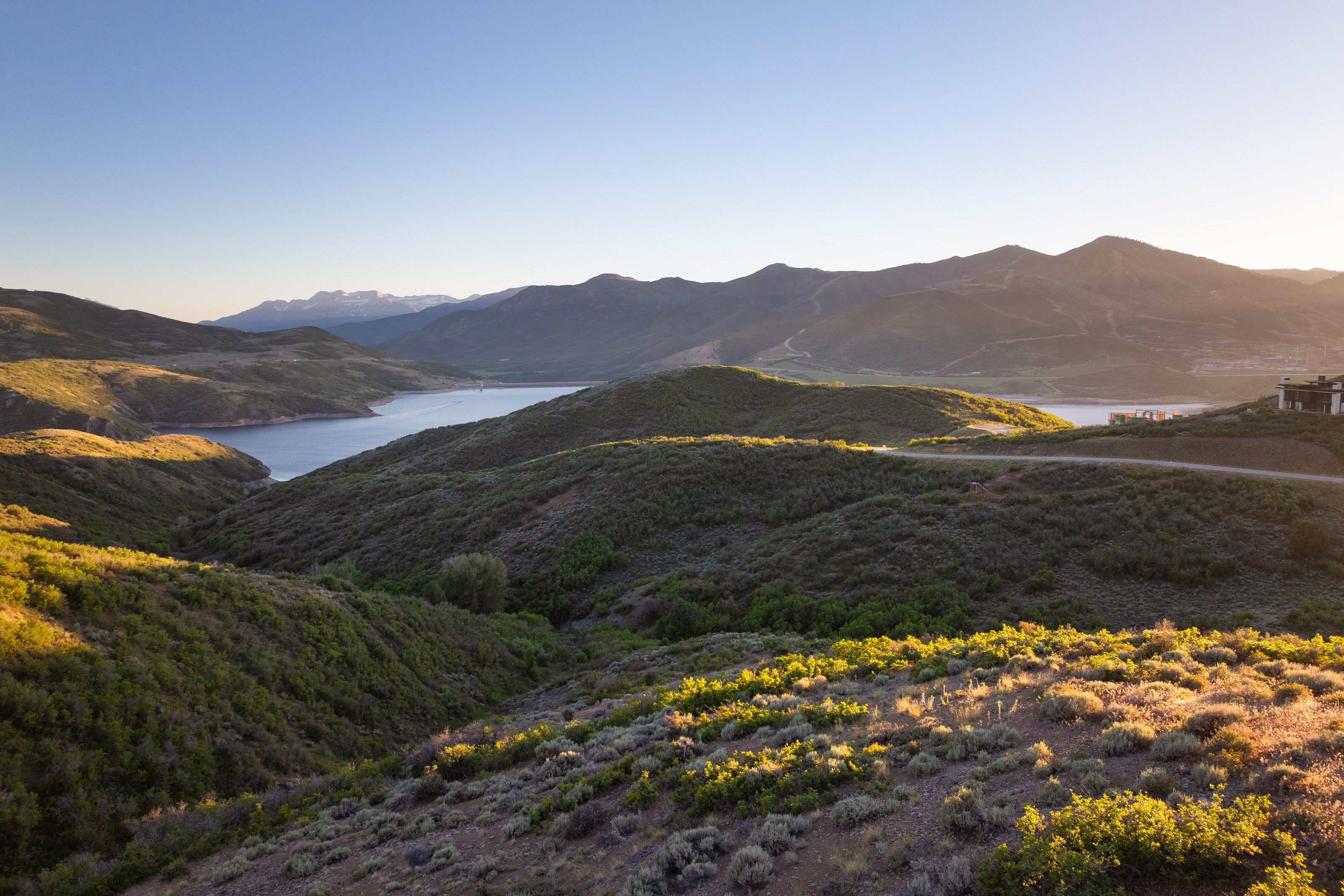 Expansive mountainous terrain featuring a large body of water, distant snow-capped peaks, and a property with a dark-toned exterior