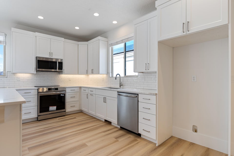 Modern kitchen featuring white shaker cabinetry, stainless steel appliances, a subway tile backsplash, and light wood-finish flooring