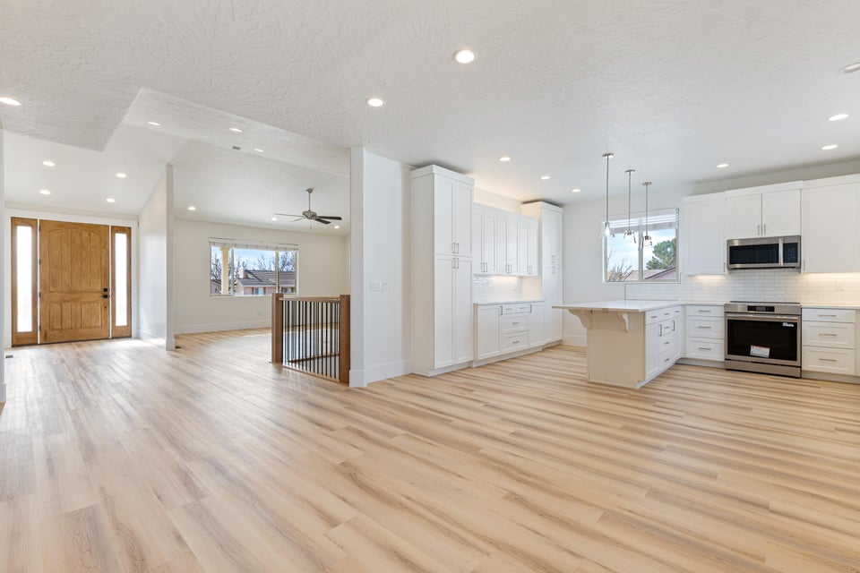 Open concept living space featuring wood-finish flooring, recessed lighting, and a kitchen with white cabinetry and stainless steel appliances