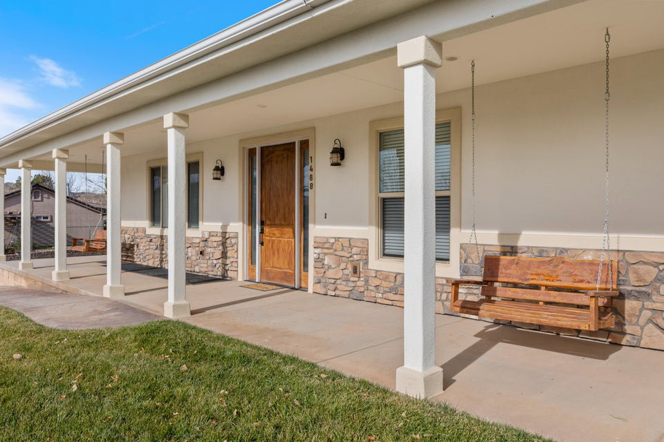 Covered front porch featuring multiple support columns, a wood-paneled entry door, two exterior wall sconces, and a stone accent wall