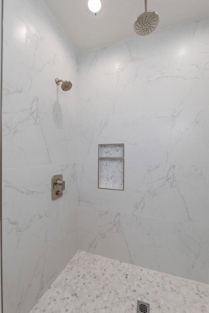 Shower featuring dual shower heads, recessed niche with tile inlay, and floor-to-ceiling marble-look tile