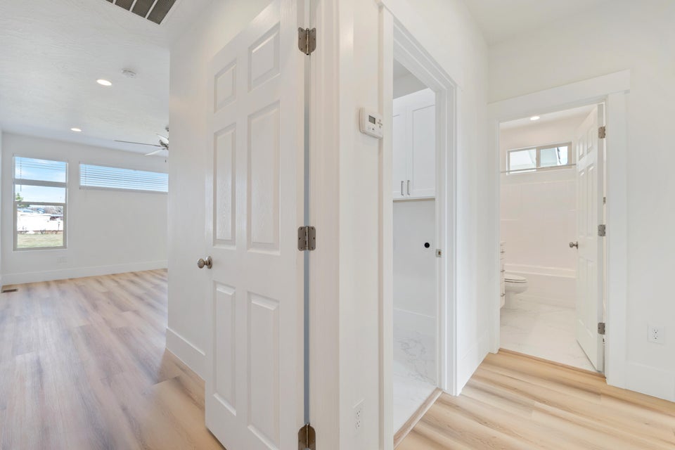 Light wood-finish flooring throughout, bright white walls, recessed ceiling lighting, and horizontal windows with blinds