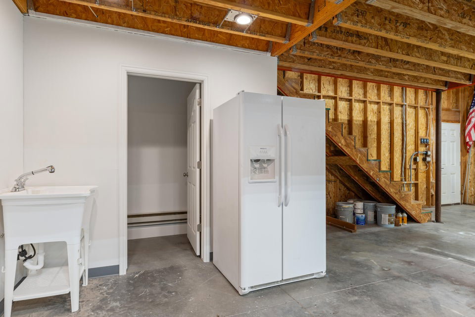 Utility area featuring a white wash basin with chrome faucet, a side-by-side refrigerator, exposed ceiling joists, and a partial staircase with wood framing