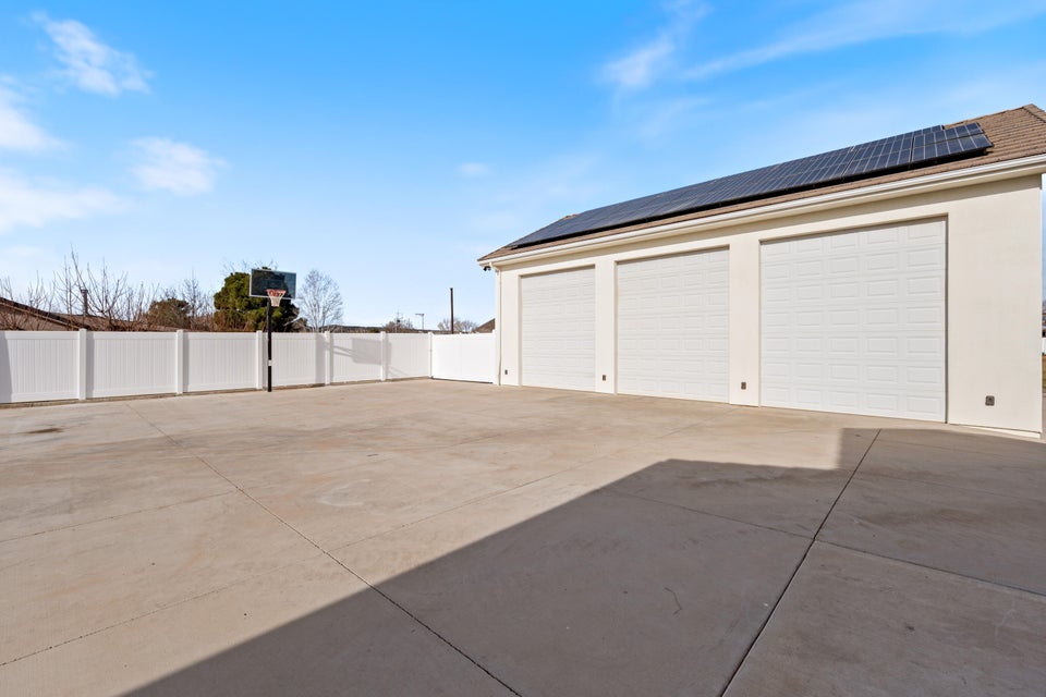 Three-car garage with white roll-up doors, solar panels, and a surrounding privacy fence