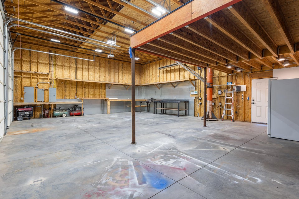 Spacious garage with exposed wood beam ceiling, concrete flooring, and multiple built-in workbenches