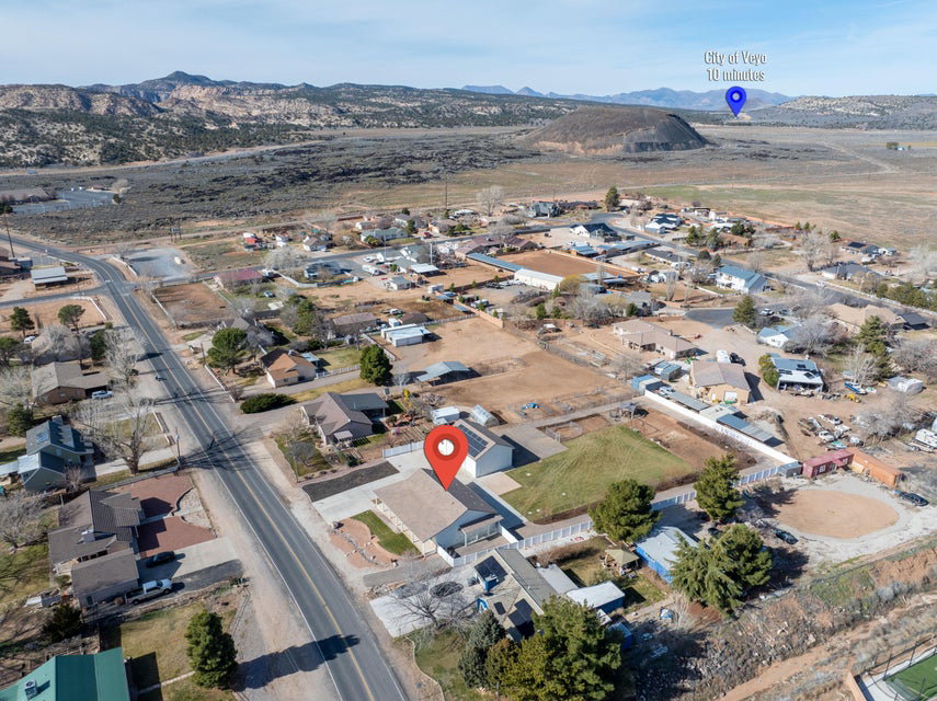 Aerial depiction of a residential property within a community setting, featuring a light-colored roof structure, surrounding open land, and nearby mountainous terrain