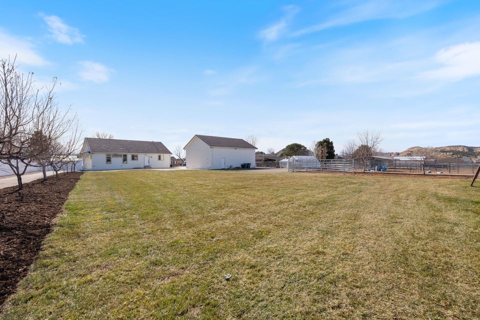 Expansive grassy yard with a white ranch-style home, detached garage, and fenced enclosures