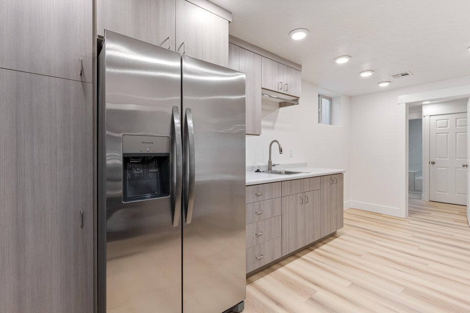 Kitchenette featuring stainless steel French door refrigerator with ice and water dispenser, light wood-finish cabinetry, light-colored countertops, stainless steel sink with gooseneck faucet, and recessed ceiling lighting