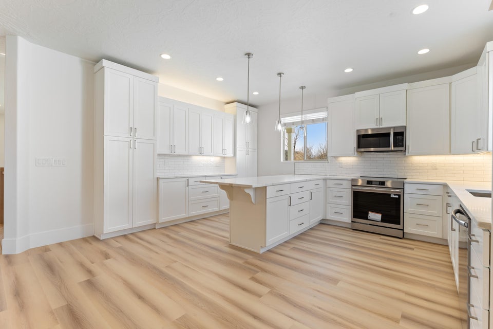 Bright kitchen featuring wood-finish flooring, white cabinetry, a central island, recessed lighting, and stainless steel appliances