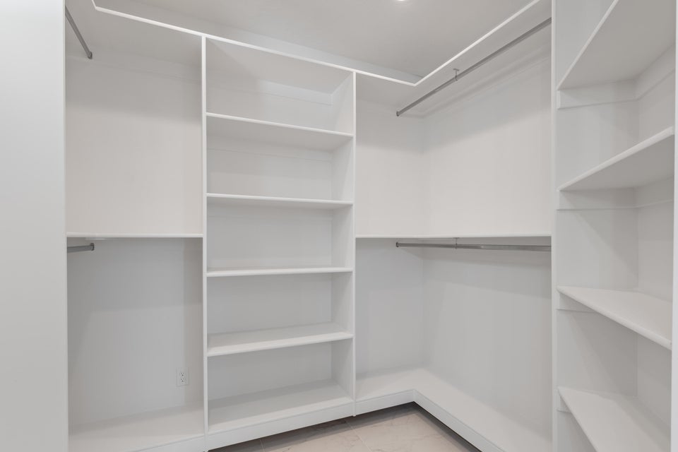 Walk-in closet featuring white built-in shelving, multiple hanging rods, and recessed lighting