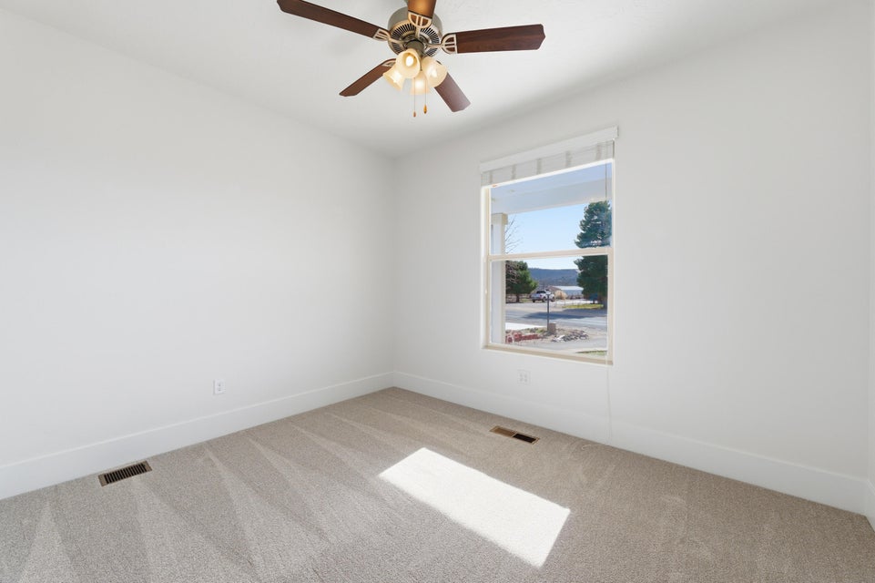 Window with exterior scenery, overhead ceiling fan with light fixture, light neutral carpet, and white baseboards