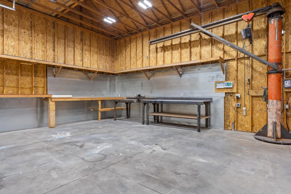 Industrial-style workspace featuring concrete flooring, raw plywood walls, high ceilings, and built-in workbenches