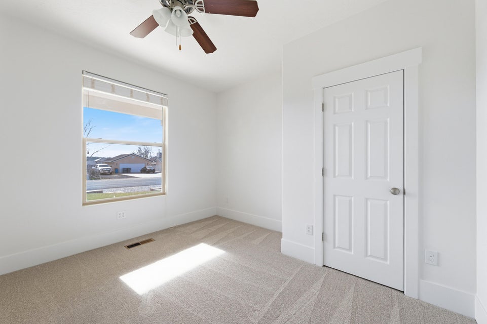 Neutral tone wall paint with a window featuring blinds, a ceiling fan with integrated lighting, and carpet flooring