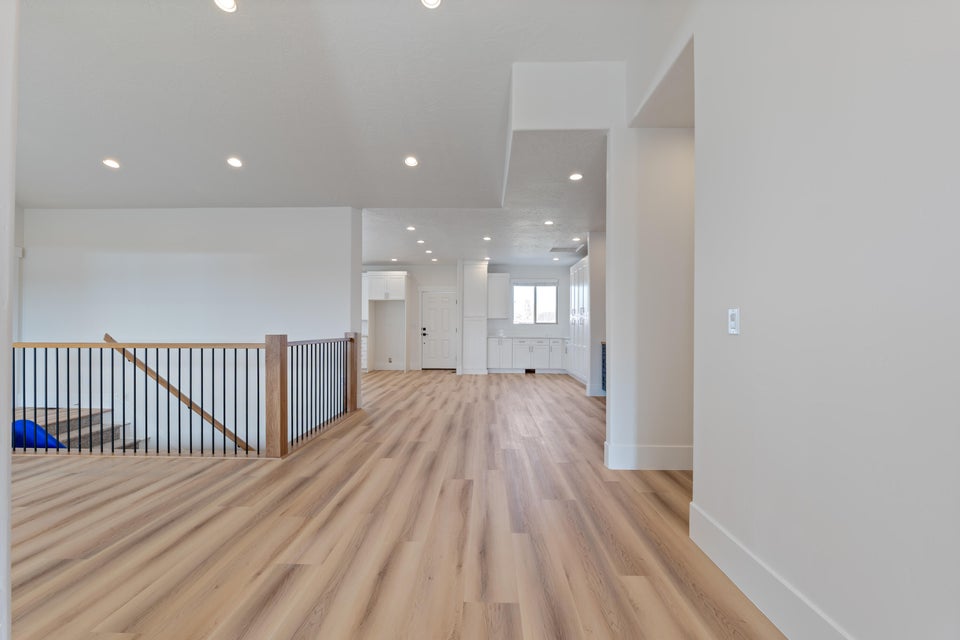 Expansive open-concept room featuring light wood-finish flooring, recessed lighting, and a modern staircase railing with wood newel posts and black balusters