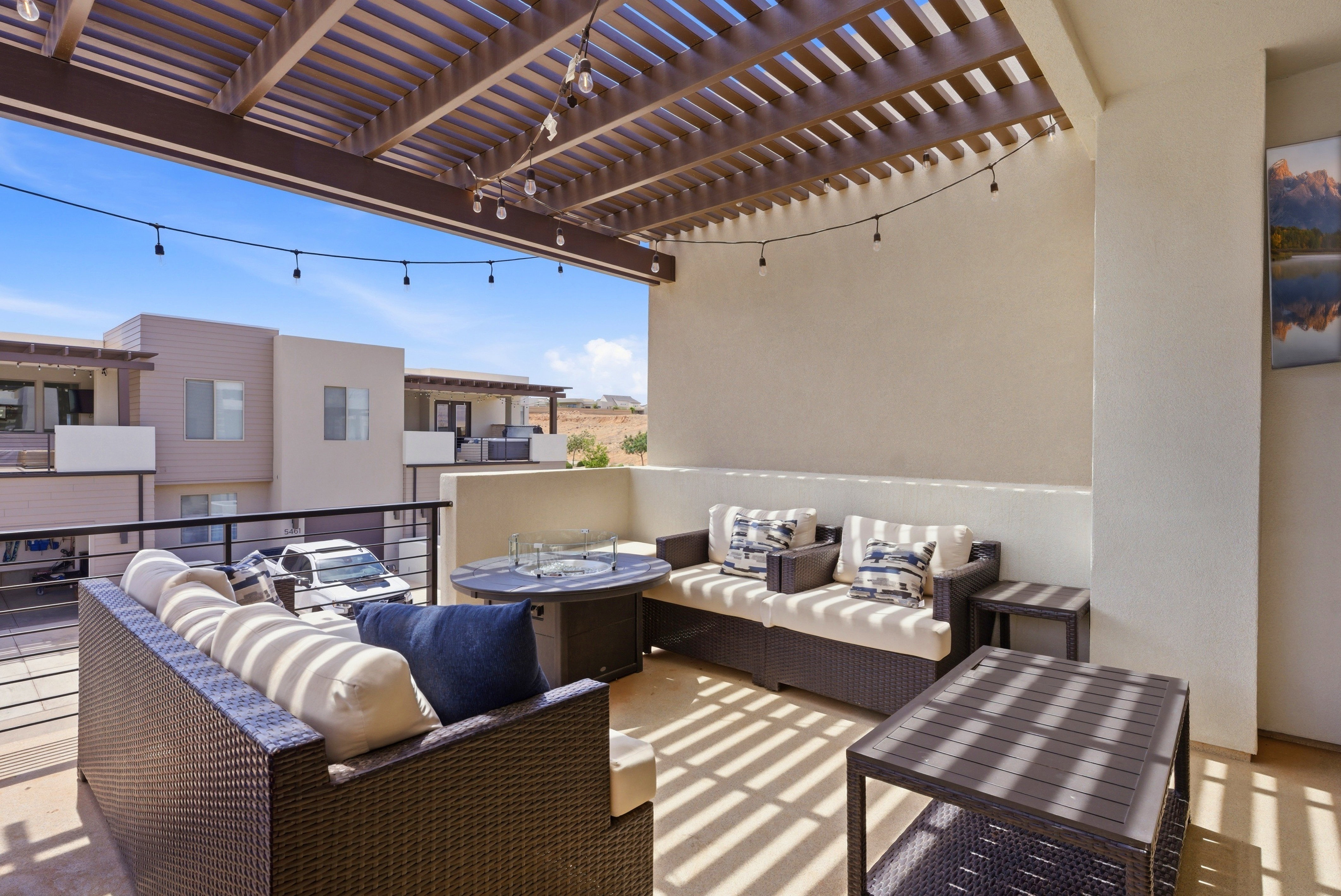 Expansive outdoor patio featuring a slatted pergola, string lighting, and stucco walls